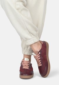 Burgunderfarbene Sneaker aus strukturiertem Stoff und glatten Lederakzenten. Mit beigen Schnürsenkeln und einer Gummisohle mit einem dezenten Muster.