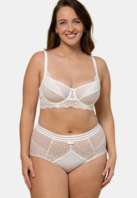 Ensemble de soutien-gorge blanc et de culotte taille haute avec de la dentelle transparente, des bords festonnés et un accent en nœud central. Bretelles réglables et texture décorative.