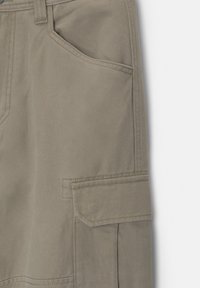 Gros plan sur la poche d'un pantalon cargo beige avec rabat et coutures doubles visibles sur un tissu résistant.