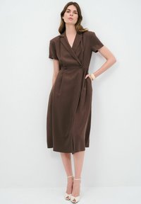 Robe marron sur mesure avec un col, des manches courtes et des poches latérales. Présente un design croisé avec des boutons et une longueur mi-genou.