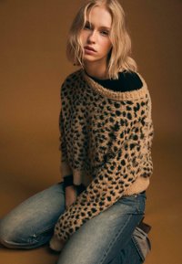 Leopardenmuster, übergroßer Pullover in Beige und Schwarz, flauschige Textur. Kombiniert mit hellblauen Jeans, die einen lockeren Schnitt haben. Schlichtes, zeitloses Design.