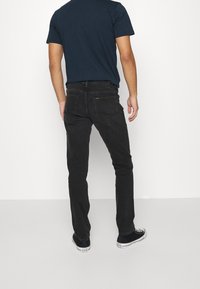 Mustat farkut slim fit -mallilla ja ompeluaccenteilla. Yhdistetty tummansinisellä t-paidalla ja mustilla lenkkareilla, näyttäen rentoa taka-näkymää.