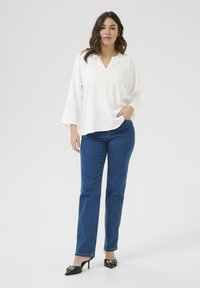 Vit, lätt blus med V-ringning och puckelryggar, kombinerad med högmidjade, raka blå jeans och svarta spetsiga klackar.