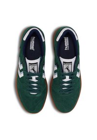 Grønne ruskinds sneakers med hvide detaljer, der har lukket tå, snørebåndsdesign og en brun gummisål. Branding på tungen.