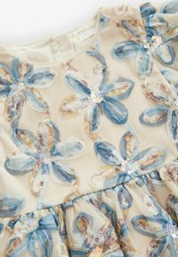 Sheer beige fabric dress with large embroidered blue and beige flowers decorated with small sequins on the petals.