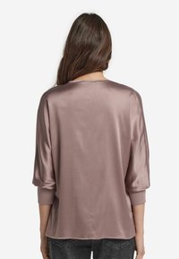 Seidiger, mauvefarbener Oberteil mit lockerer Passform, 3/4-Ärmeln und rundem Ausschnitt, der eine glatte Textur und minimale Nahtdetails aufweist.