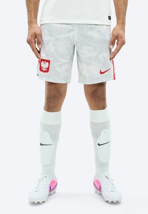 Jalad, mis kannavad valgeid ja halli Poola jalgpallipükse, valgeid Nike sääriseid ja valgeid ketsid roosa ja lilla aktsendiga.