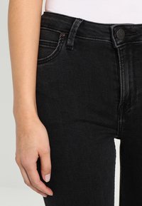 Jeans de mezclilla negra con una cintura alta, bolsillos frontales y costuras en contraste. El material tiene un acabado suave y ligeramente texturizado.