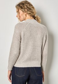 Helles beige gestricktes Sweatshirt mit einem strukturierten Muster, Raglanärmeln und einer lockeren Passform, kombiniert mit dunklen Jeans.