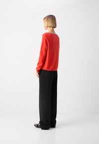 Pull rouge avec un col rond, assorti à un pantalon noir ample. Texture lisse et manches longues, vu de dos.