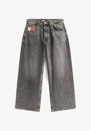 Palaidi kelnės plačiu sijonu, pagamintos iš išblukusio juodo denim, su priekiniais mygtukais, penkiais kišenėmis ir maža raudona-balta etikete ant galinės kišenės.