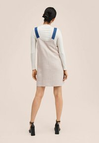 Robe sans manches en tissu léger texturé, bretelles en denim bleu et coupe droite. Portée sur un haut blanc à manches longues et manches ajustées.