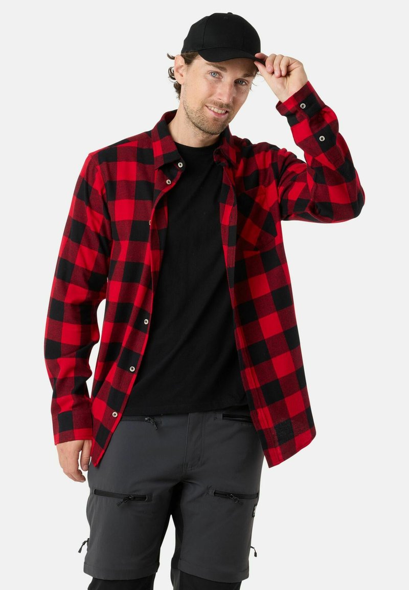 Rood en zwart geblokt flanellen overhemd, lange mouwen, met knopen aan de voorkant, gedragen over een zwart T-shirt, gecombineerd met donkere shorts en een zwarte pet.