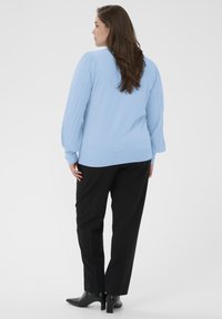 Világoskék pulóver bordázott, ballon ujjakkal, fekete egyenes szárú nadrággal és fekete hegyes orrú bokacsizmával párosítva. Sima textúra.