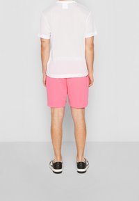 Bílé síťované tričko s krátkými rukávy, v kombinaci s růžovými šortkami. Černé boty s jednoduchým designem a bílou podrážkou.