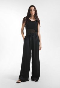 Mustat leveälahkeiset housut, joissa on nyörivyötärö, yhdistetty tiukasti istuvaan mustaan yläosaan, jossa on teksturoitu muotoilu ja pyöreä pääntie.