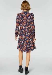 Długa, granatowa sukienka z długim rękawem, w kwiatowy wzór w pomarańczowe i kremowe odcienie, z wcięciem w talii i lekko rozkloszowanym dołem.