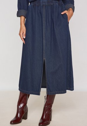 Gonna di jeans con vita elastica, lunghezza al ginocchio, colore blu scuro, tasche laterali e uno spacco frontale. Accoppiata con stivali con tacco bordeaux.