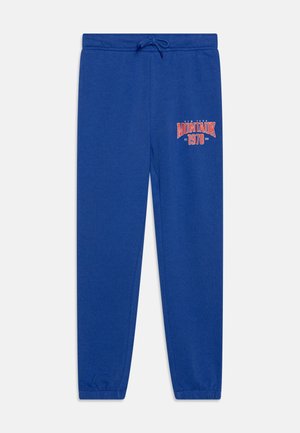 Blå joggingbukser med elastisk talje og manchetter, med teksten "Montauk 1978" i rød og hvid på det øvre venstre lår.