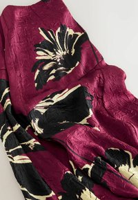 Bordeaux gekleurde stof met bloemenpatroon en zwarte en crèmekleurige accenten. Gestructureerd, gekreukt oppervlak met gedurfde bloemontwerpen en kleurcontrast.
