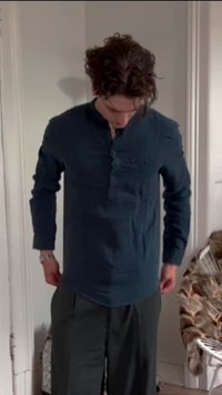 Camisa de mangas compridas azul-escura com placket de botões, bolso no peito esquerdo e um ajuste descontraído, usada com calças cinzas.