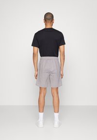 Chemise noire à manches courtes avec un col rond, associée à un short rayé gris et blanc. Le modèle porte des baskets blanches et des chaussettes montantes.