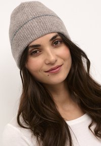 Pelēks adīts beanie ar noapaļotu augšpusi un zilu horizontālu svītru. Audums izskatās mīksts un teksturēts, parādot ribotu rakstu.