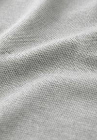 Tessuto grigio chiaro con una superficie intrecciata e texture; la visione ravvicinata mostra i dettagli fini e i fili intrecciati. Aspetto morbido e leggermente stropicciato.