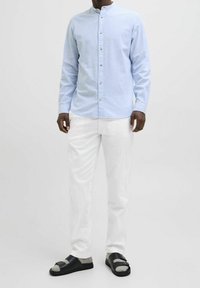 Světle modrá košile s dlouhým rukávem a stojáčkem, šedé knoflíky, bílé kalhoty a černé sandály se šedými detaily. Hladká textura látky.