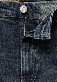 Tmavě modré džíny z denimu s předním zapínáním na knoflík, viditelným šitím a tradičním zipem. Tkanina má texturovaný povrch.
