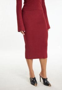Jupe en tricot côtelé rouge avec une silhouette ajust�ée, longueur genoux, associée à des mules à talons hauts noires avec un accent doré sur l'orteil.