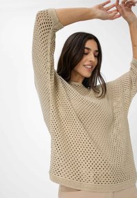 Lichtbeige gebreide trui met een losse, oversized pasvorm, brede halslijn en open weefpatroon. Korte, aansluitende mouwen.