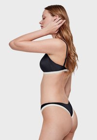 Conjunto de bikini negro que incluye un sujetador triangular con una banda blanca en contraste, diseño elegante y hardware mínimo, destacando texturas suaves.