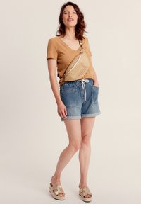 T-shirt v-neck beige, pantaloni shorts in denim blu con risvolti, sandali platform beige, e una borsa a tracolla in paglia, caratterizzata da un design elegante e una tracolla regolabile.