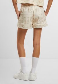 Beige gemusterte Shorts mit elastischem Bund, die ein dezentes Blumenmuster aufweisen, getragen mit weißen Socken und Sneakers.