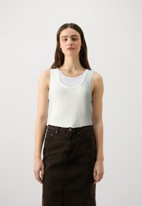 Lys grå, ermeløs strikket topp med teksturert finish lagd over en hvit ribbet tank. Kombinert med et mørkt denim blyantskjørt.