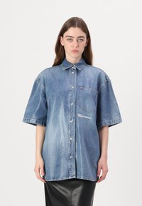 Μπλε τζιν oversized πουκάμισο με κοντά μανίκια, κουμπιά μπροστά και τσέπη στο στήθος. Διαθέτει λεπτομέρεια λογότυπου στο μπροστά μέρος.