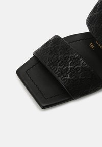 Sandale noire avec un bout carré et une large bride texturée présentant un motif embossé subtil.