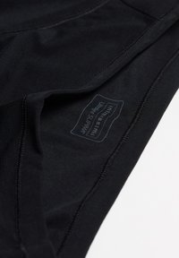 Zwarte stoffen kledingstukken met een gladde textuur, voorzien van stiksels en een label met verzorgingsinstructies en merkinformatie.