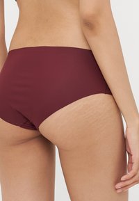 Burgundiška aukšto liemens bikini dugnas iš lygaus audinio, turintis subtilią tekstūrą ir be siūlių dizainą, suteikiantis minimalų užnugario uždengimą.