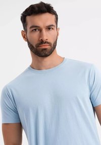 Světle modré bavlněné tričko s krátkými rukávy a kulatým výstřihem. Hladká textura, minimalistický design a přiléhavý tvar, který ukazuje ležérní vzhled.