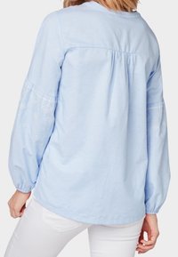 Hellblaue Bluse mit langen Puffärmeln, bestickten Blumenmotiven und gerafftem Rückenteil. Hergestellt aus weichem, leichtem Stoff.