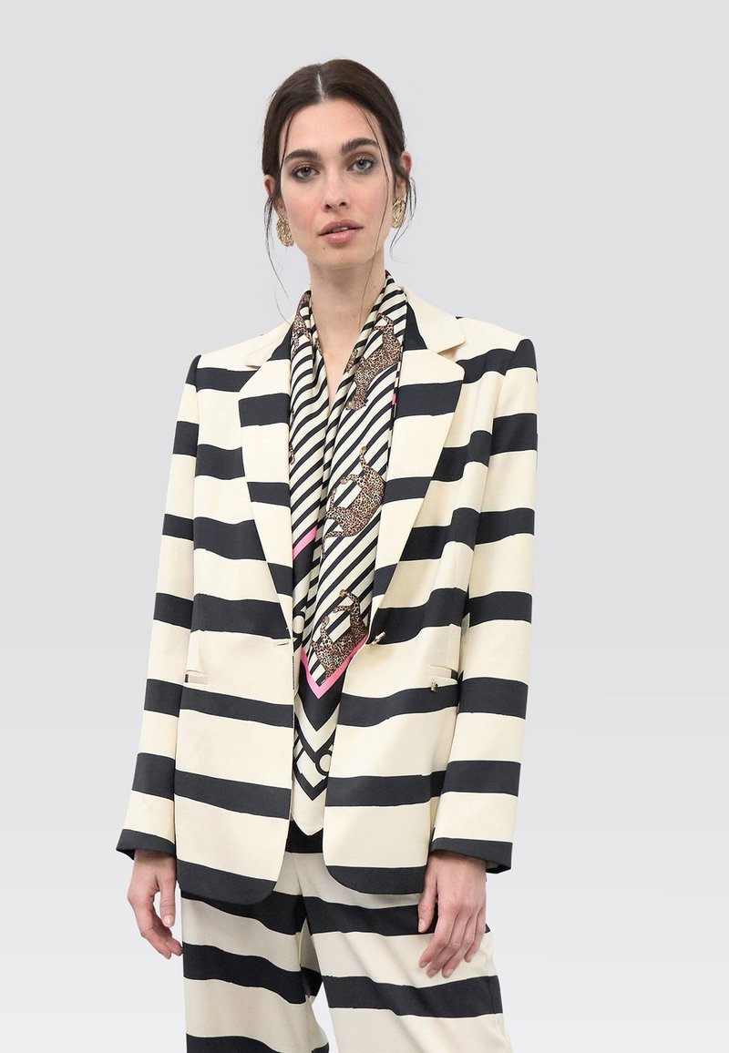 Stribet blazer i creme- og sort stof med to forlommer. Kombineret med et mønstret tørklæde med sorte og pink accenter.