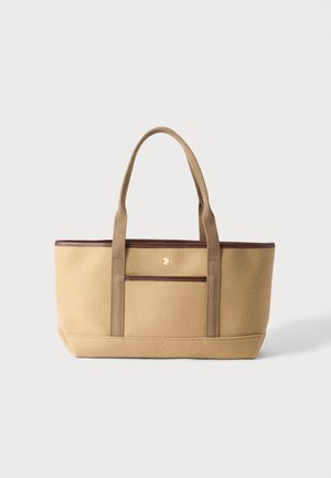 Sac cabas beige avec garniture marron, deux longues poignées en tissu et une poche avant sur un fond clair.