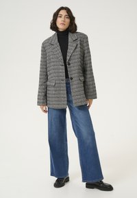 Houndstooth patterned blazer in black and white, single-breasted with two front pockets, paired with wide-leg blue jeans and black shoes.