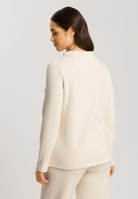 Cremfarbener Fleece-Oberteil mit hohem Kragen, langen Ärmeln und lockerer Passform. Glatte Textur mit subtilen Nähdetails, kombiniert mit passenden Hosen.