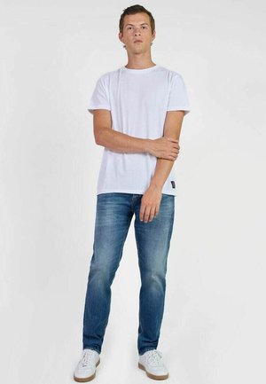 T-shirt blanc à col rond, jeans droits bleus et baskets blanches. Design simple, coupe décontractée, avec peu de détails et un lavage léger sur les jeans.