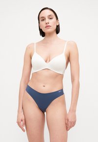 Bijela bešavna bralette sa podesivim naramenicama i dubokim izrezom, u kombinaciji s thong gaćicama u tamnoplavoj boji s niskim strukom, koje imaju mali logotip.
