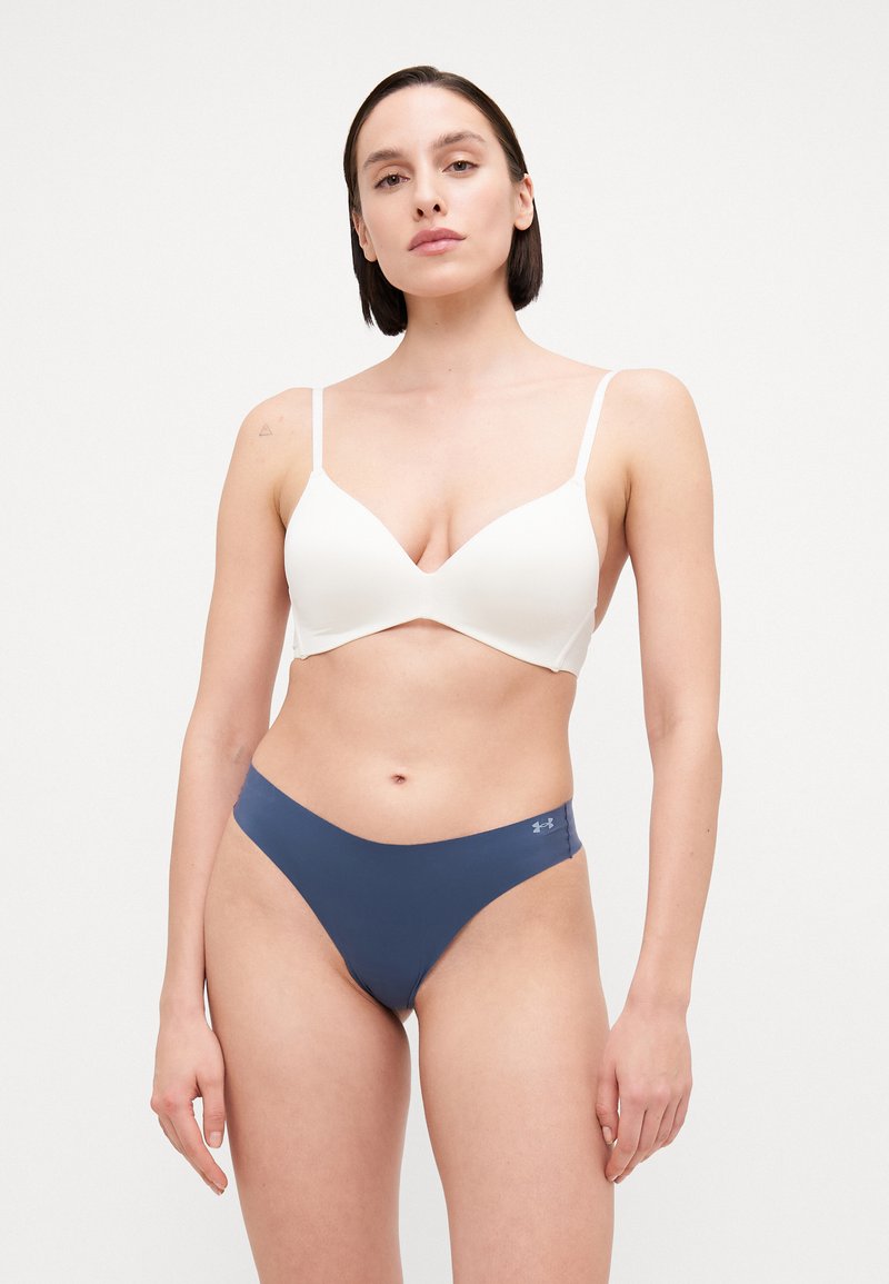 Bijela bešavna bralette sa podesivim naramenicama i dubokim izrezom, u kombinaciji s thong gaćicama u tamnoplavoj boji s niskim strukom, koje imaju mali logotip.