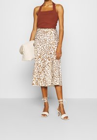 Top halter de canalé marrón, falda midi blanca con patron de manchas marrones, y sandalias de tacón con tiras blancas. Bolso acolchado beige claro.